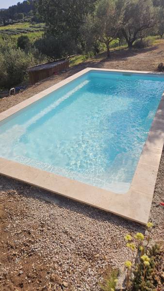 Réalisation d'une piscine en coque sur fond incliné avec margelles travertin chez un client dans le Var sur la commune de Cotignac